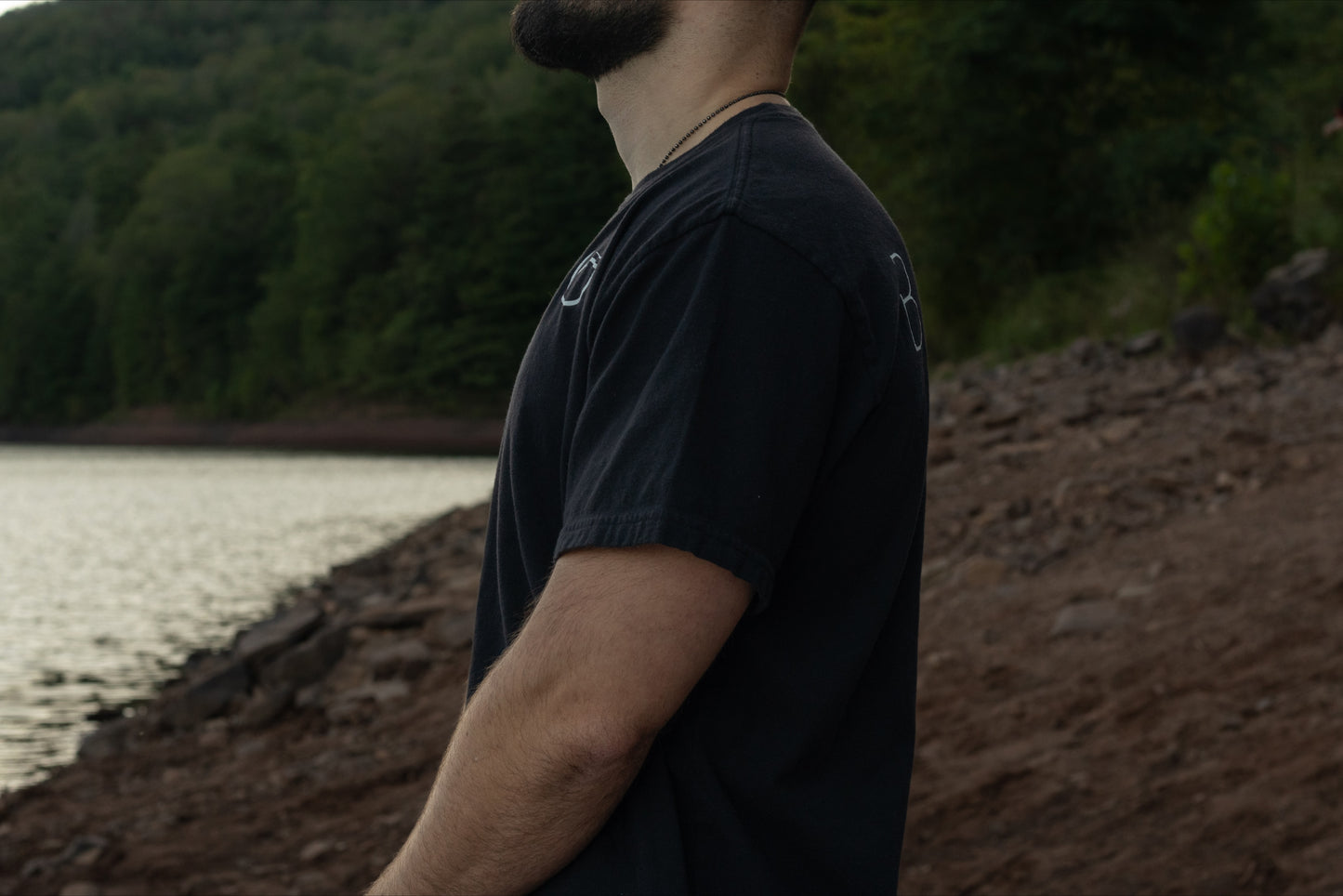 A person standing profile with the black t shirt by Breath with the logo on the chest and brand name across the back, displaying the drape of the shirt. 