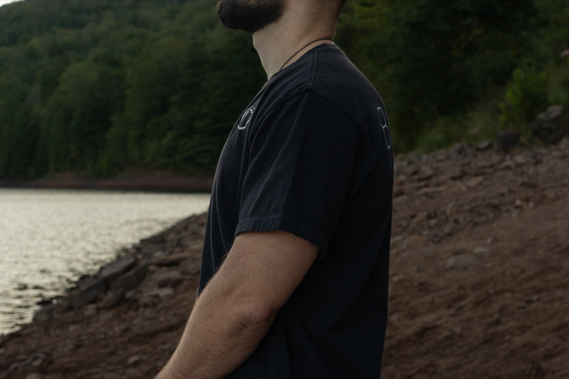 A person standing profile with the black t shirt by Breath with the logo on the chest and brand name across the back, displaying the drape of the shirt. 